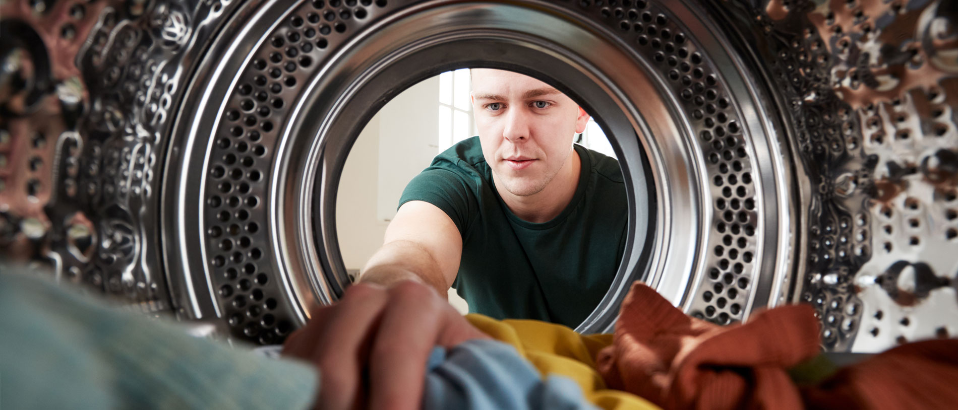 Perspektive aus dem Inneren der Wäschetrommel einer Waschmaschine: Mann greift in die Wäsche