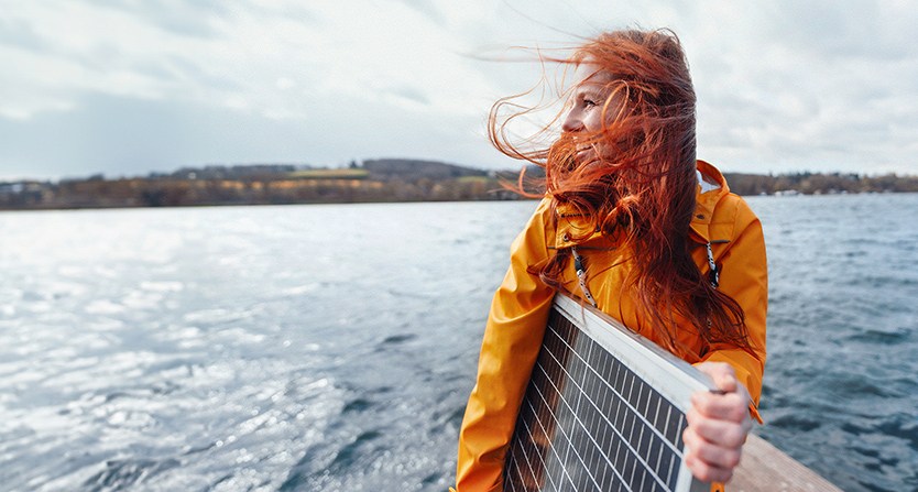 Frau mit Solar-Panel bei Wind auf einem Steg am Wasser