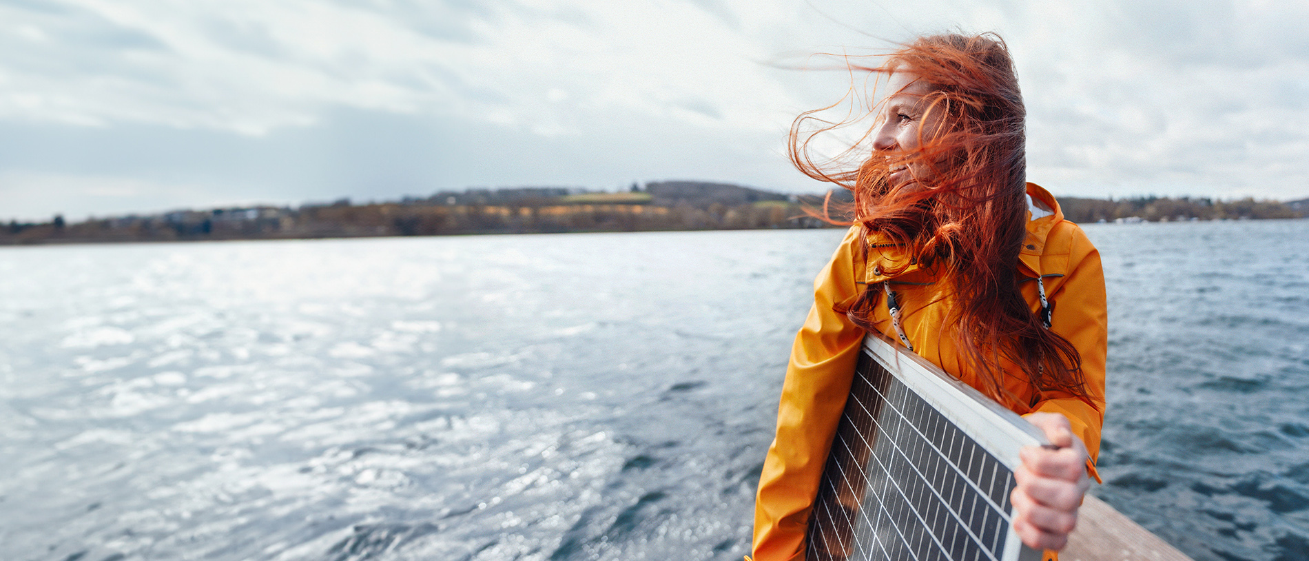 Frau mit Solar-Panel bei Wind auf einem Steg am Wasser