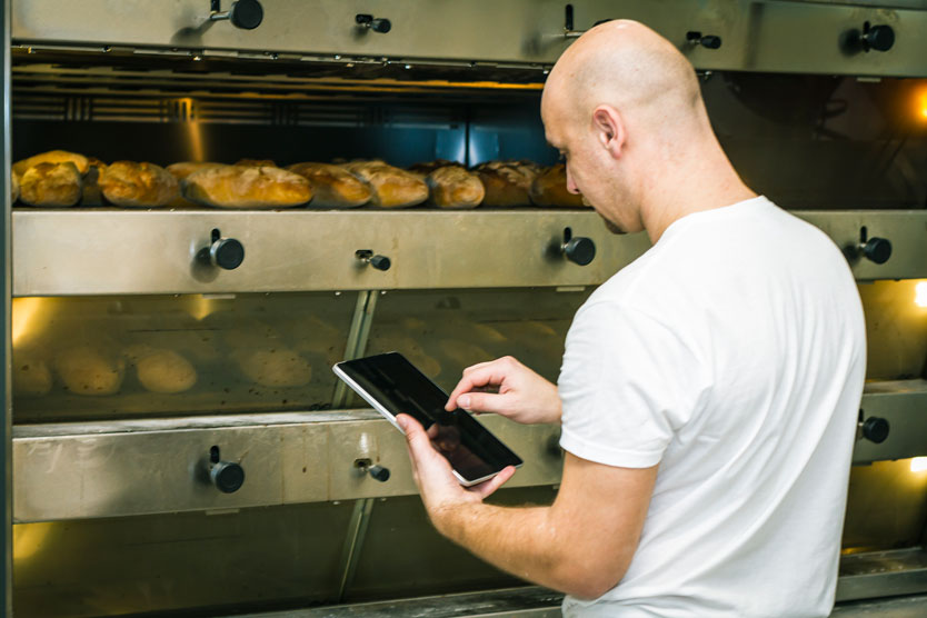 Abwärme-Investitionen; Bäcker mit Tablet PC vor Ofen
