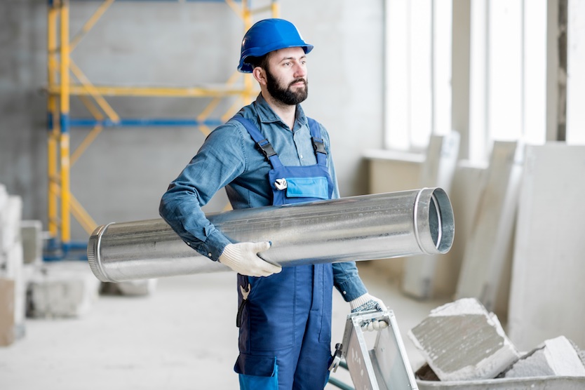 Ein Bauarbeiter steht mit einem Lüftungsrohr auf der Baustelle in einem Gebäude