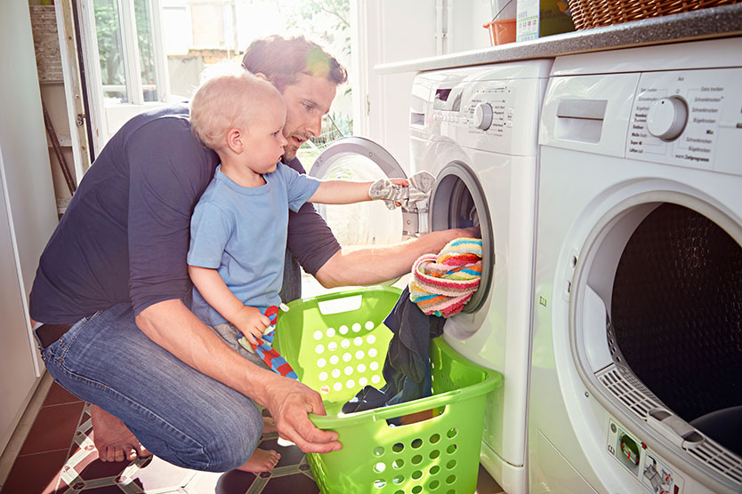 Vater und Sohn füllen Wäsche in stromsparende Waschmaschine