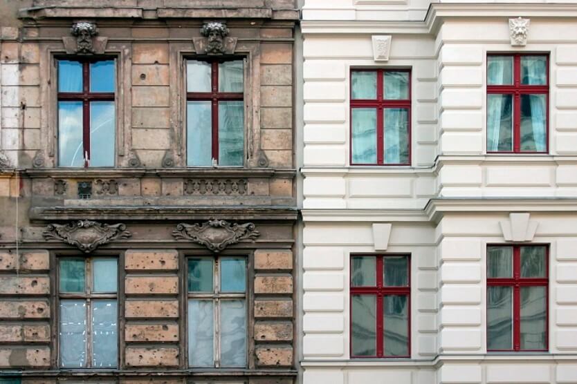 Zwei nebeneinander stehende Altbauten mit einer brüchigen und einer sanierten Fassade symbolisieren energieeffiziente Sanierung