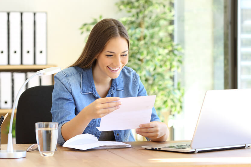 Lächelnde, junge Frau liest einen Brief am Schreibtisch