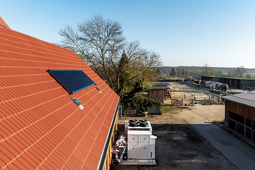 Wärmepumpen-Anlage vor Bauernhaus und Solarthermie- und Photovoltaik-Flächen auf dem Dach.